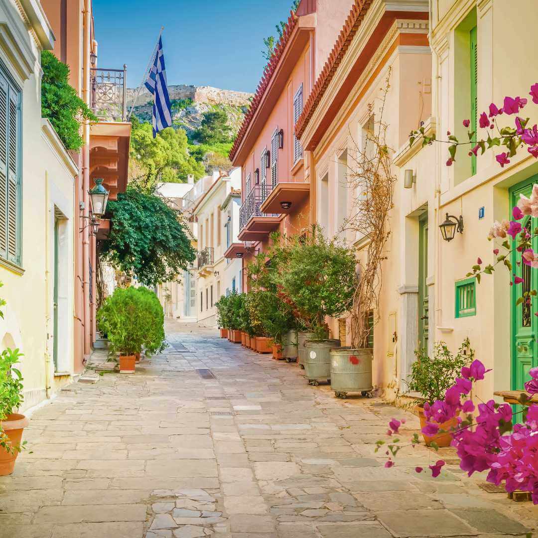 Una piccola strada lastricata piena di fiori nel quartiere di Placa con la collina dell'Acropoli sullo sfondo, Atene, Grecia