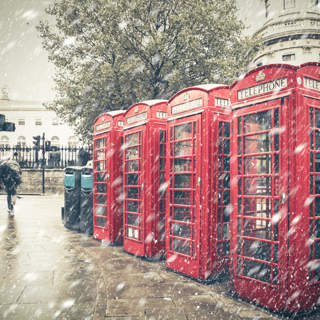 Winter London street scene with iconic red phone booths with snow falling