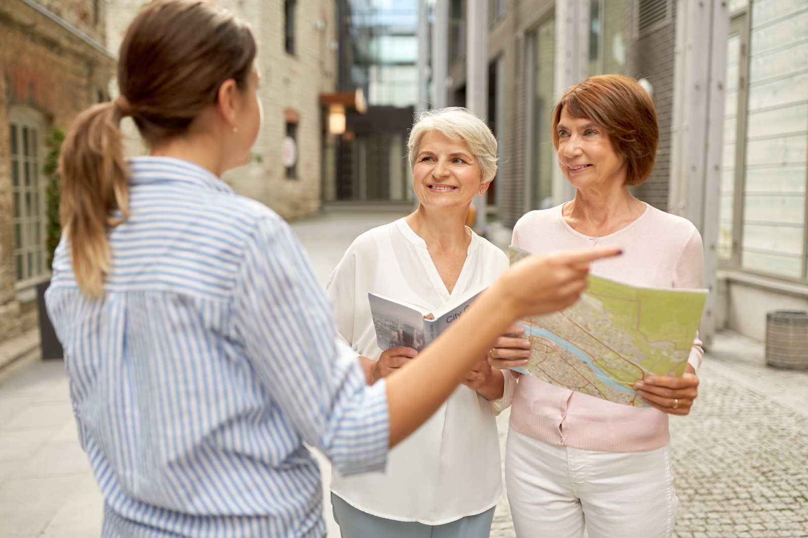 Tourismus-, Reise- und Freundschaftskonzept - Passantin zeigt älteren Frauen mit Stadtführer und Karte auf der Tallinner Straße den Weg