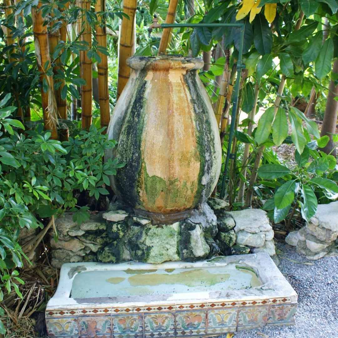 Image show a large earthenware pot with running water with large bamboo stems in background at Ernest Hemingway's house in Key West