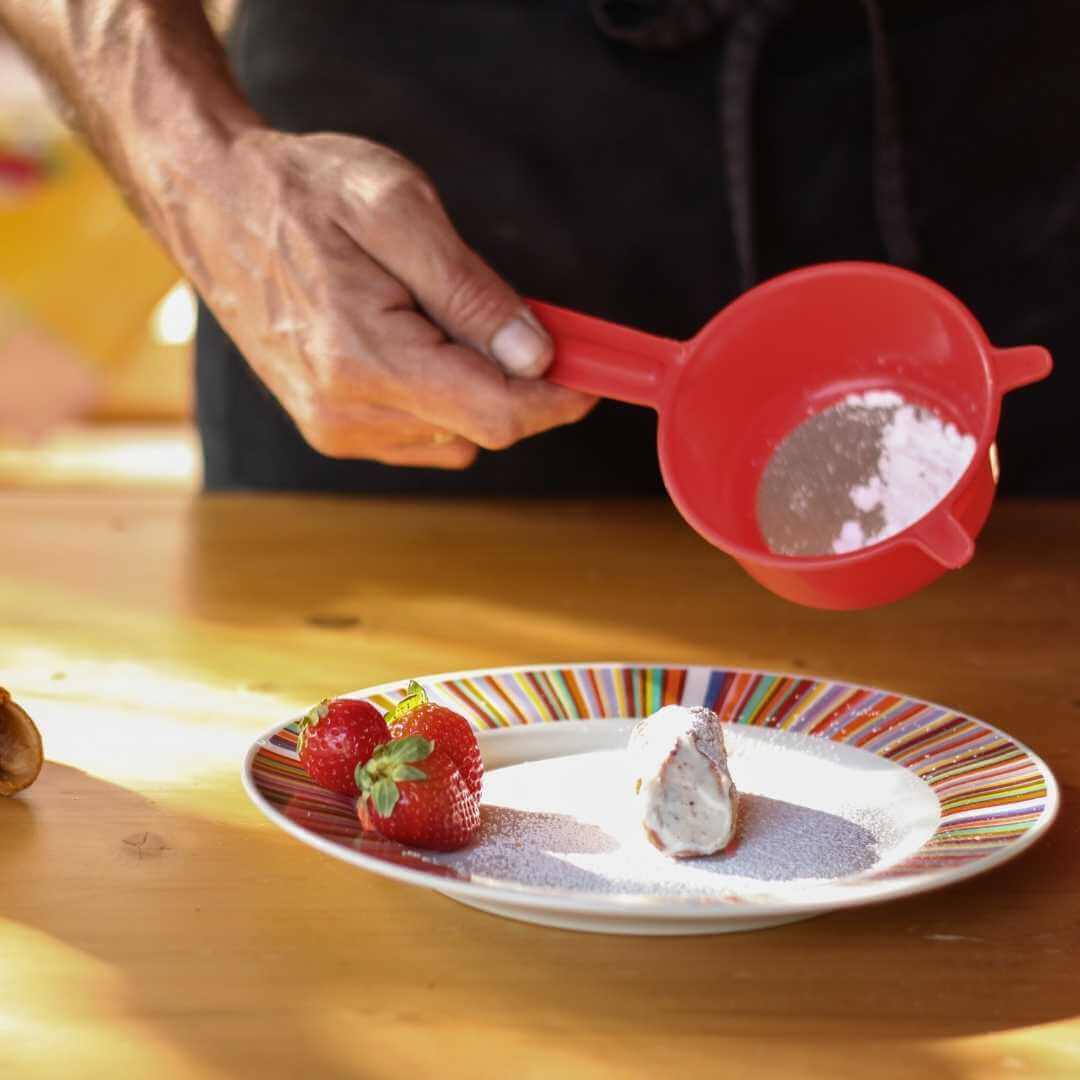 Una persona che cosparge i cannoli appena cotti con zucchero a velo