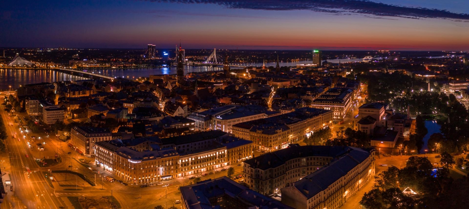 Vista panorámica de la ciudad nocturna de Riga al atardecer con la iglesia de San Pedro y el río Daugava en primer plano.  Atardecer mágico sobre la ciudad.