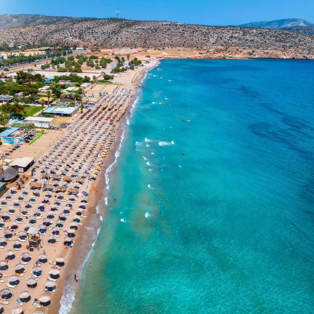 Vista aerea del resort sulla spiaggia di Varkiza, sulla costa meridionale di Atene, Attica, Grecia, con ombrelloni allineati accanto al mare turchese