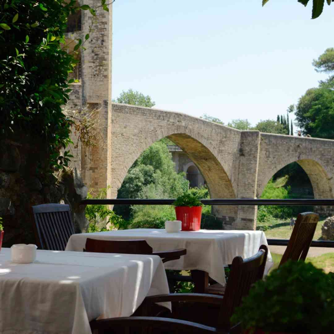 Schattige Terrasse des Restaurants Pont Vell mit atemberaubendem Blick auf die mittelalterliche Brücke in Besalu