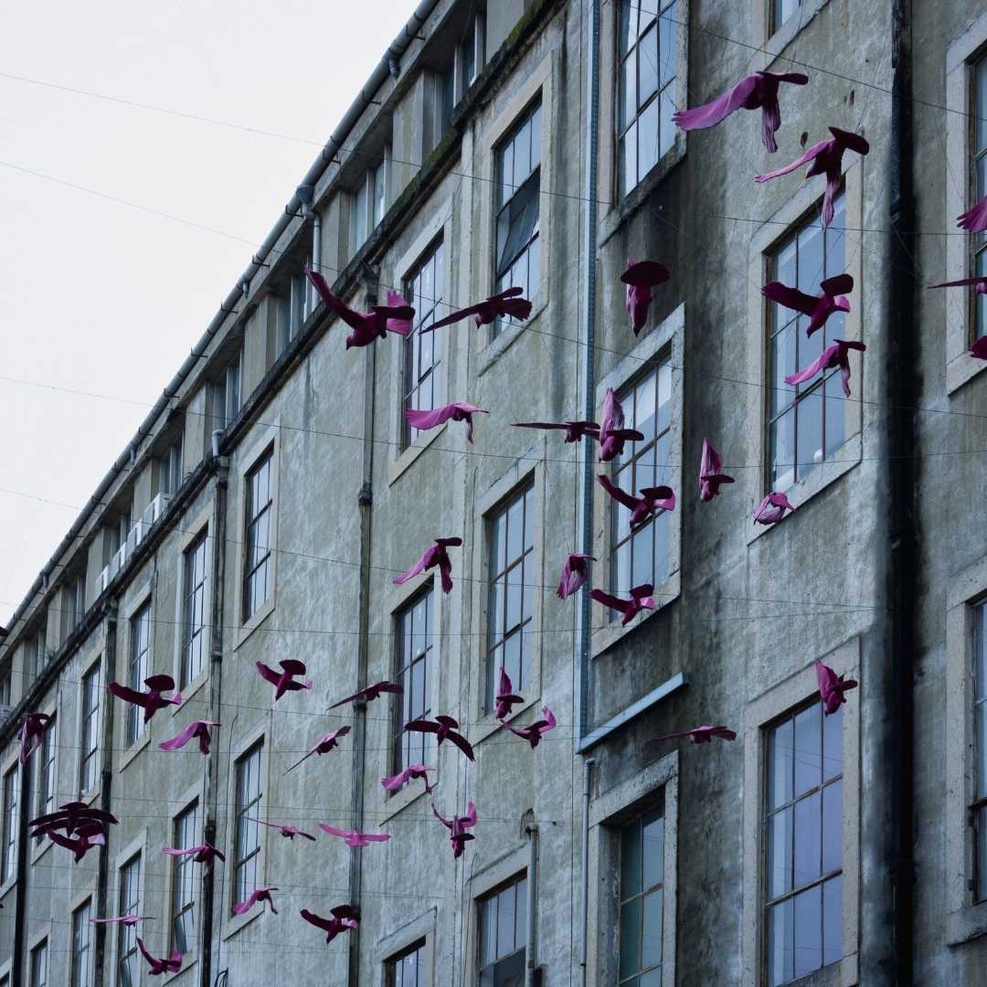 Старый фасад фабрики с искусственными фиолетовыми птицами висит в пасмурный день в знаменитом районе Лиссабона. Креативное оформление заброшенной промышленной площадки