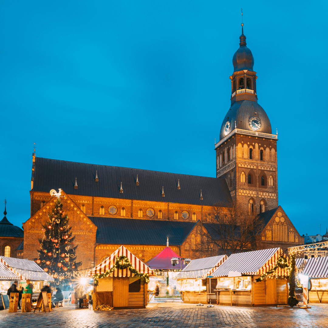Riga, Lettland. Weihnachtsmarkt am Domplatz mit Rigaer Dom. Weihnachtsbaum und Handelshäuser. Berühmtes Wahrzeichen in der Winterabendnacht im Beleuchtungslicht