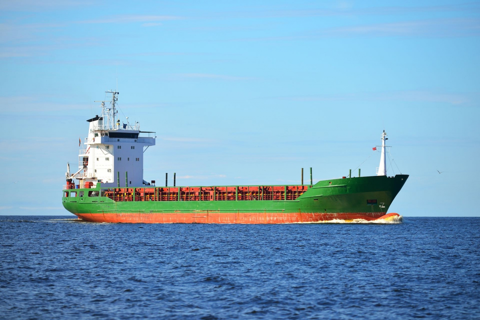 Buque de carga general verde descargado navegando en un mar tranquilo cerca de un puerto en Letonia