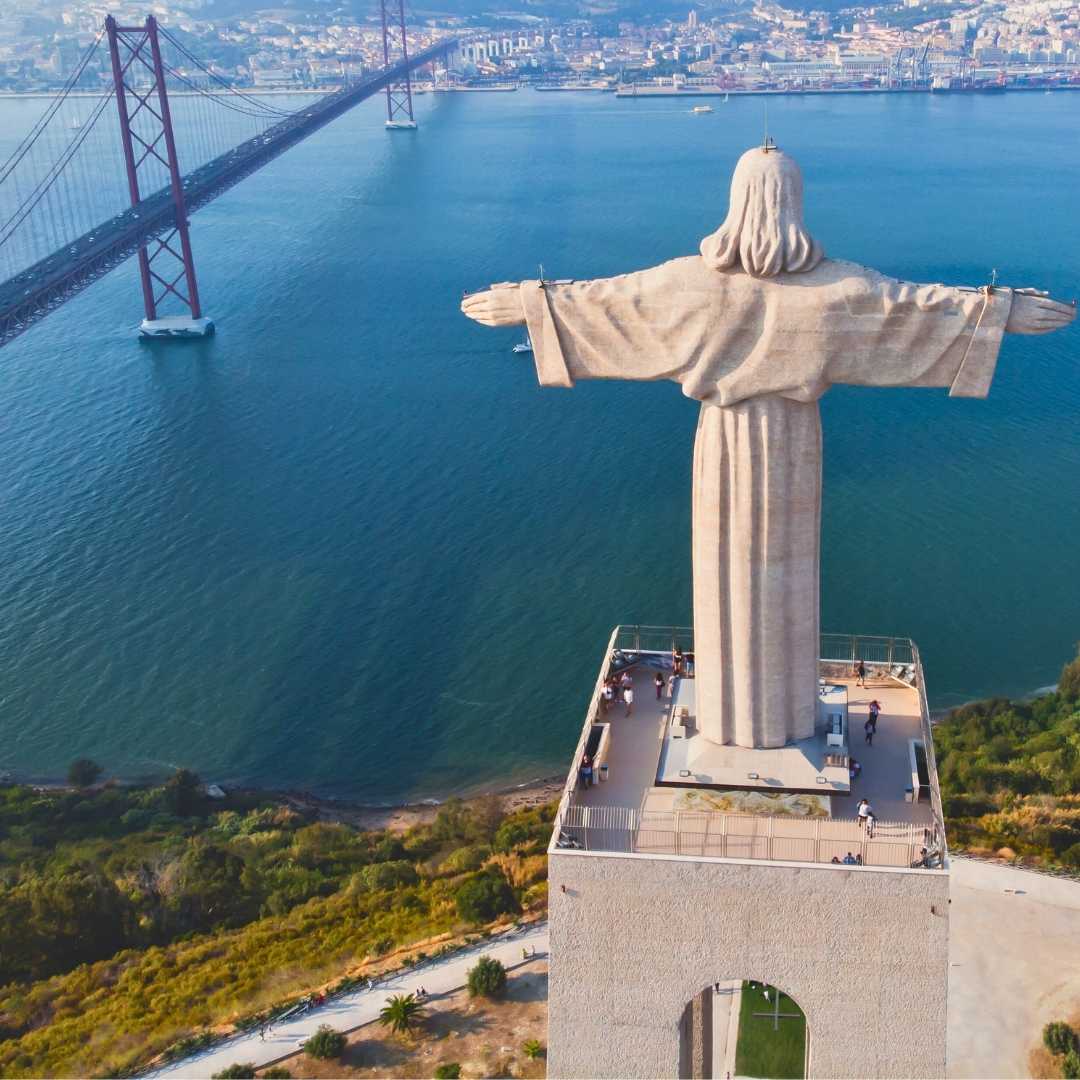 Vista aerea del drone del Santuario di Cristo Re, Cristo Rei, Almada, Lisbona, con il ponte sospeso 25 de Abril e il fiume Tago in una soleggiata giornata estiva