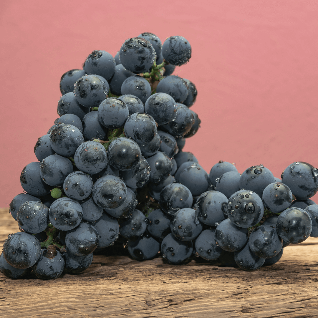 Красивое вино Кадарка из винограда на старом дубовом деревянном столе и фоне красной стены