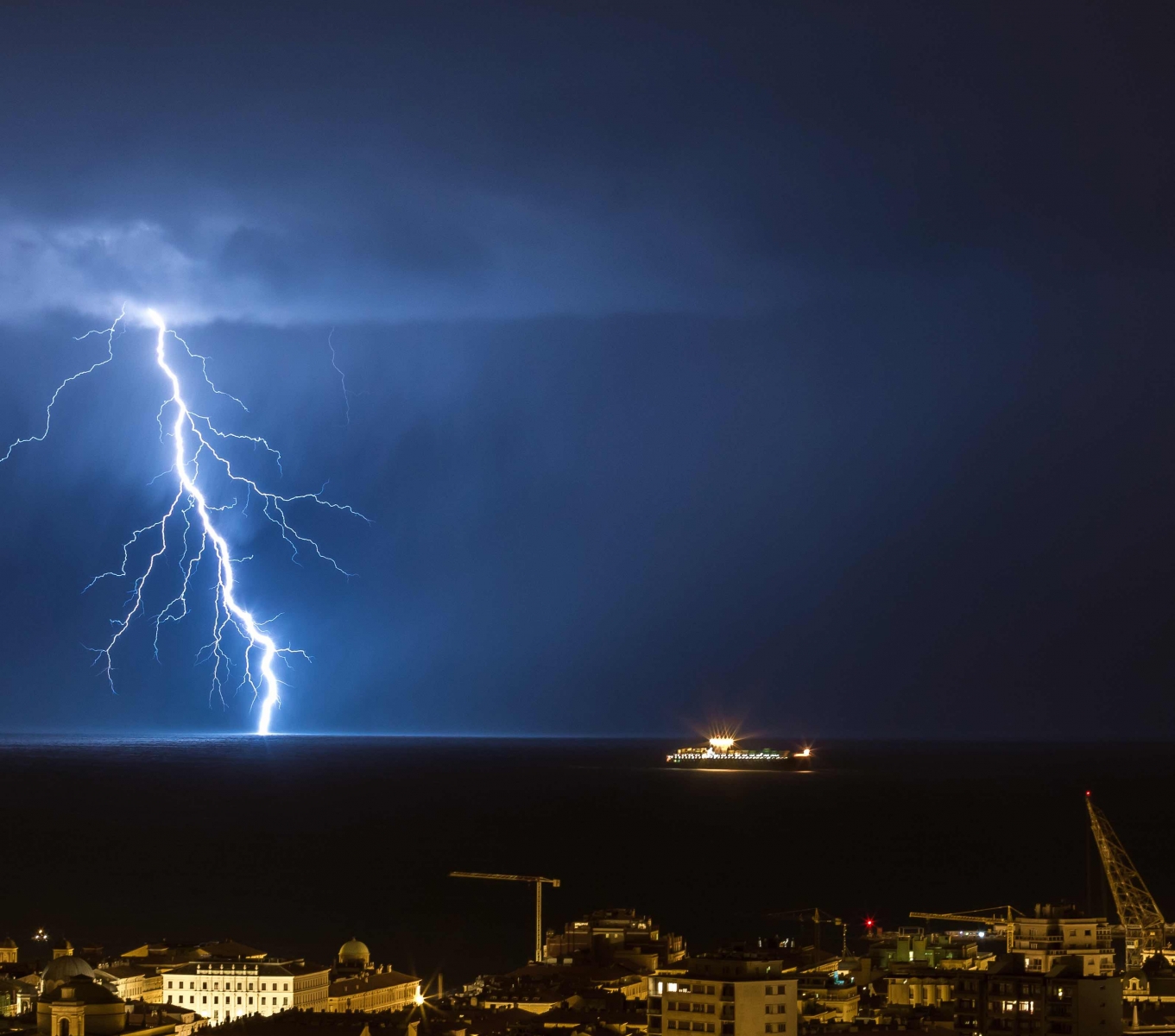 Enormes relámpagos de nube a tierra golpean el horizonte de las luces de la ciudad de Trieste