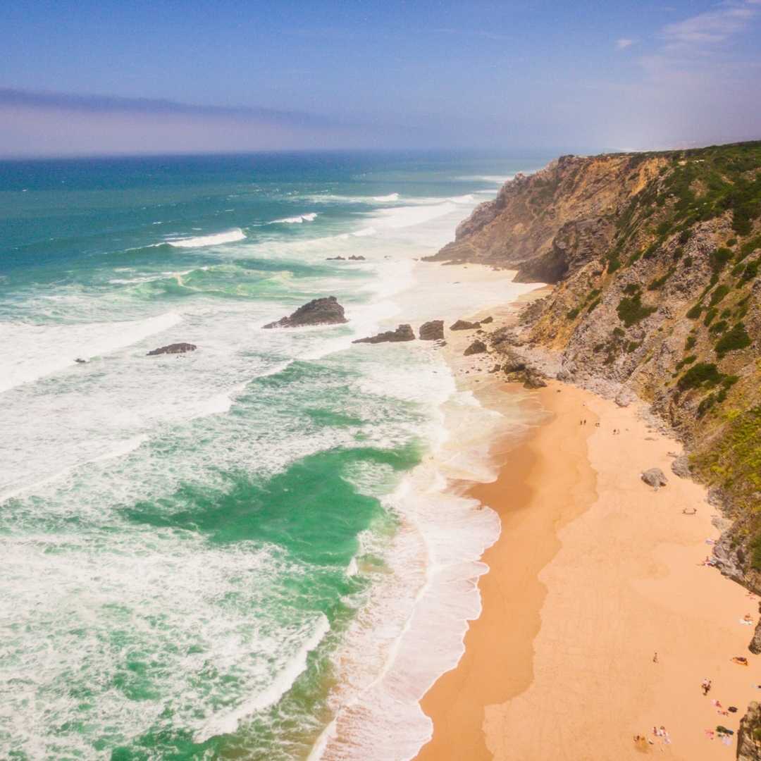 Вид с воздуха на людей, отдыхающих на пляже Прайя-да-Адрага в Португалии, Альмокагеме, Синтра